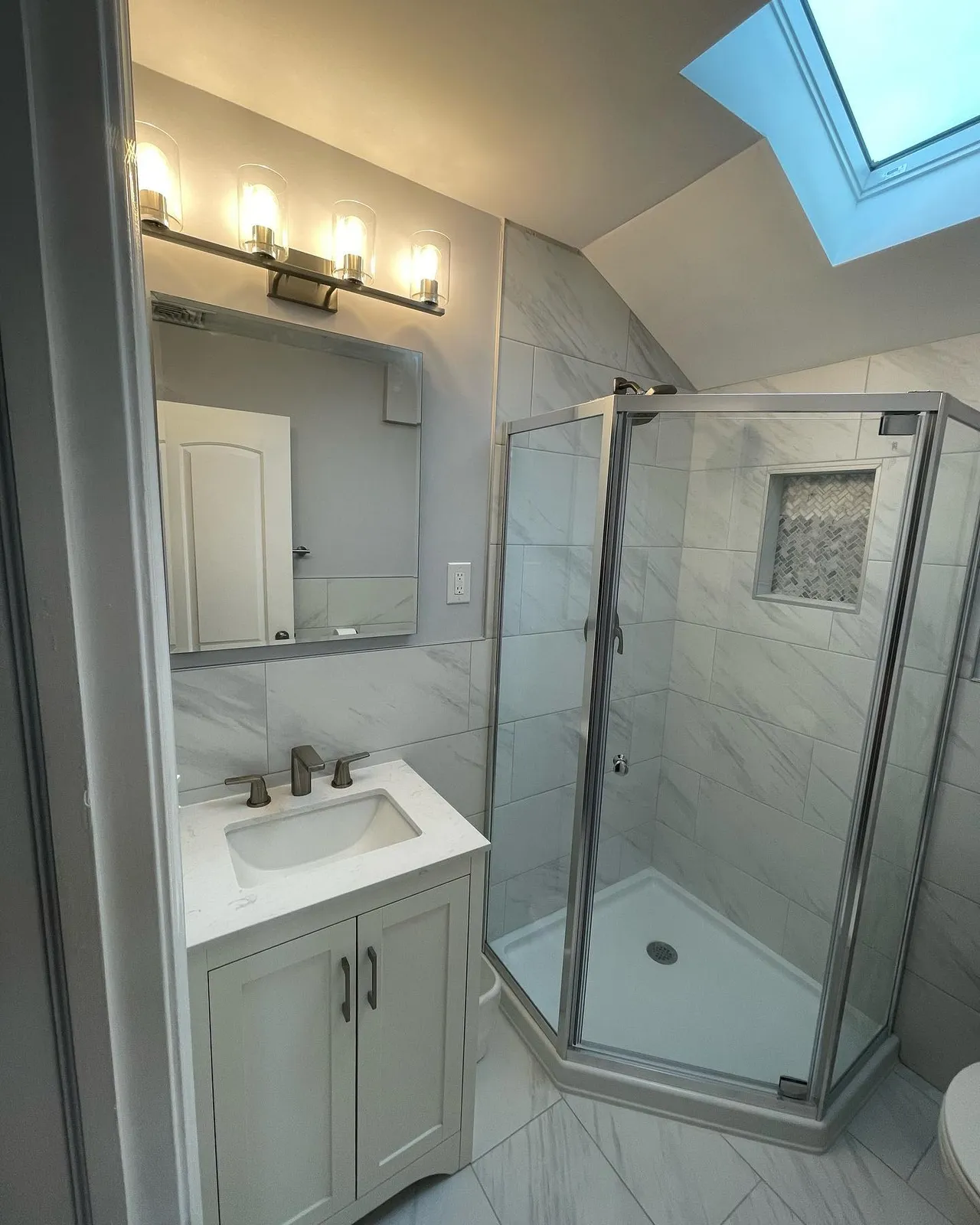 Attic bathroom with corner shower, skylight, and marble tile