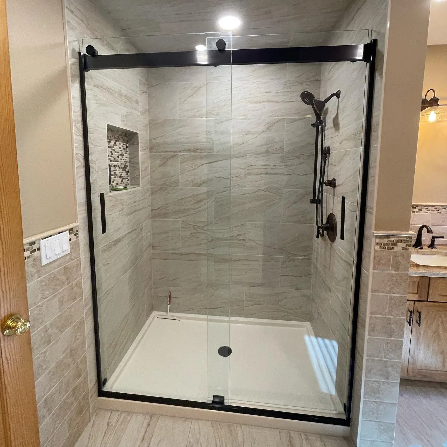 Glass sliding shower with black frame, stone tile, and mosaic niche