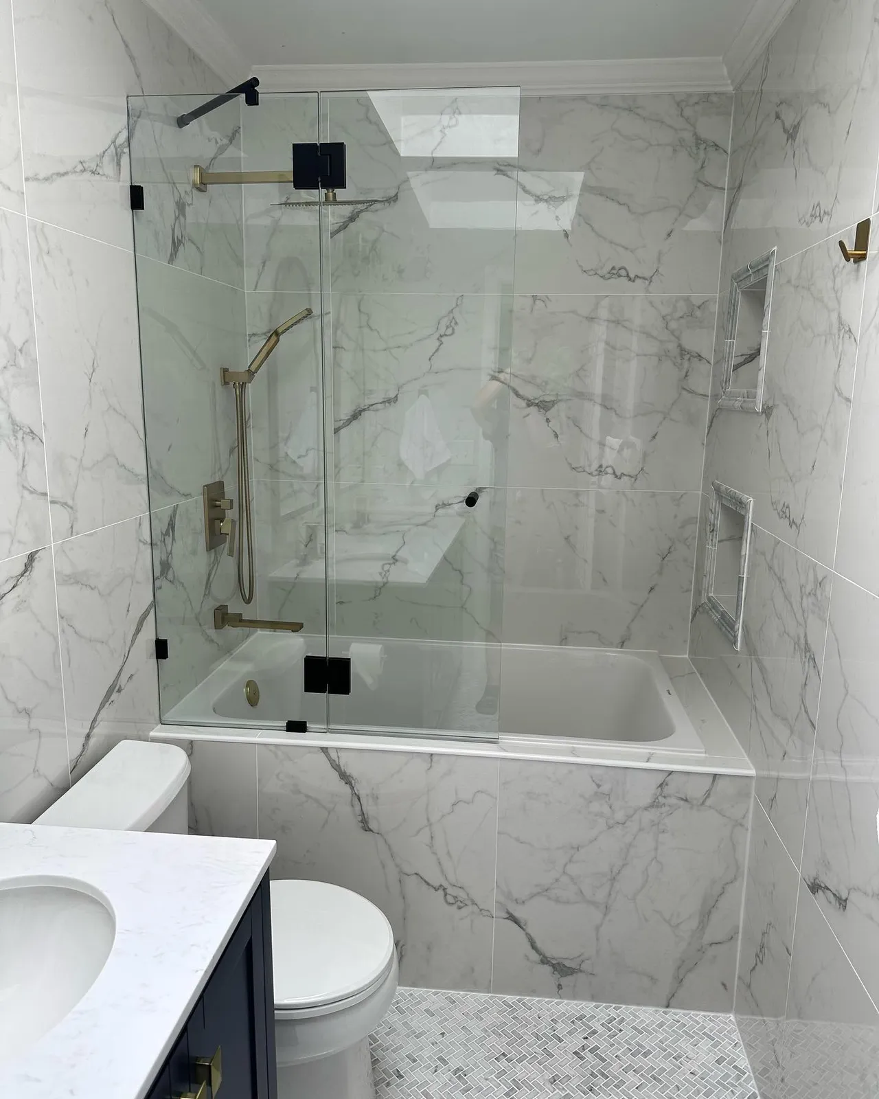 Marble bathroom with glass tub and shower, gold hardware, and navy vanity
