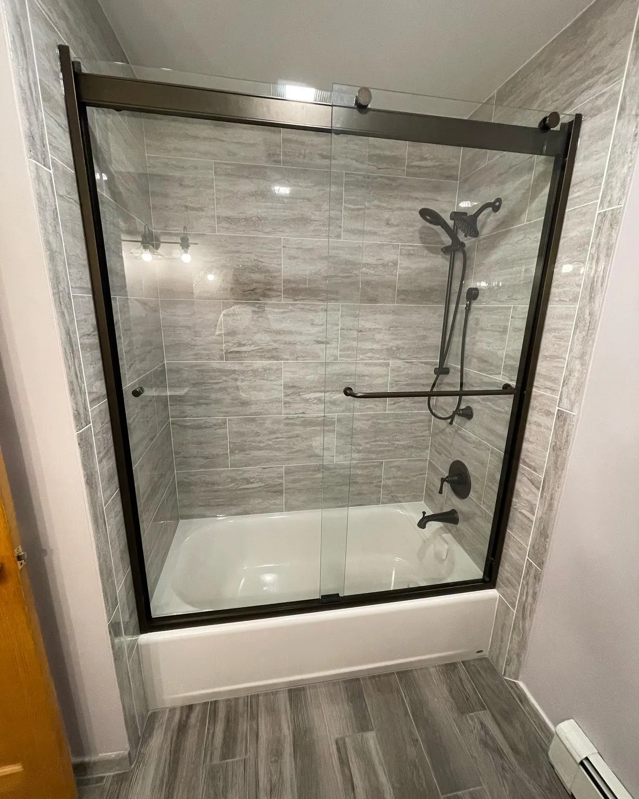 Tub and shower combo with gray tile and wood-look floor
